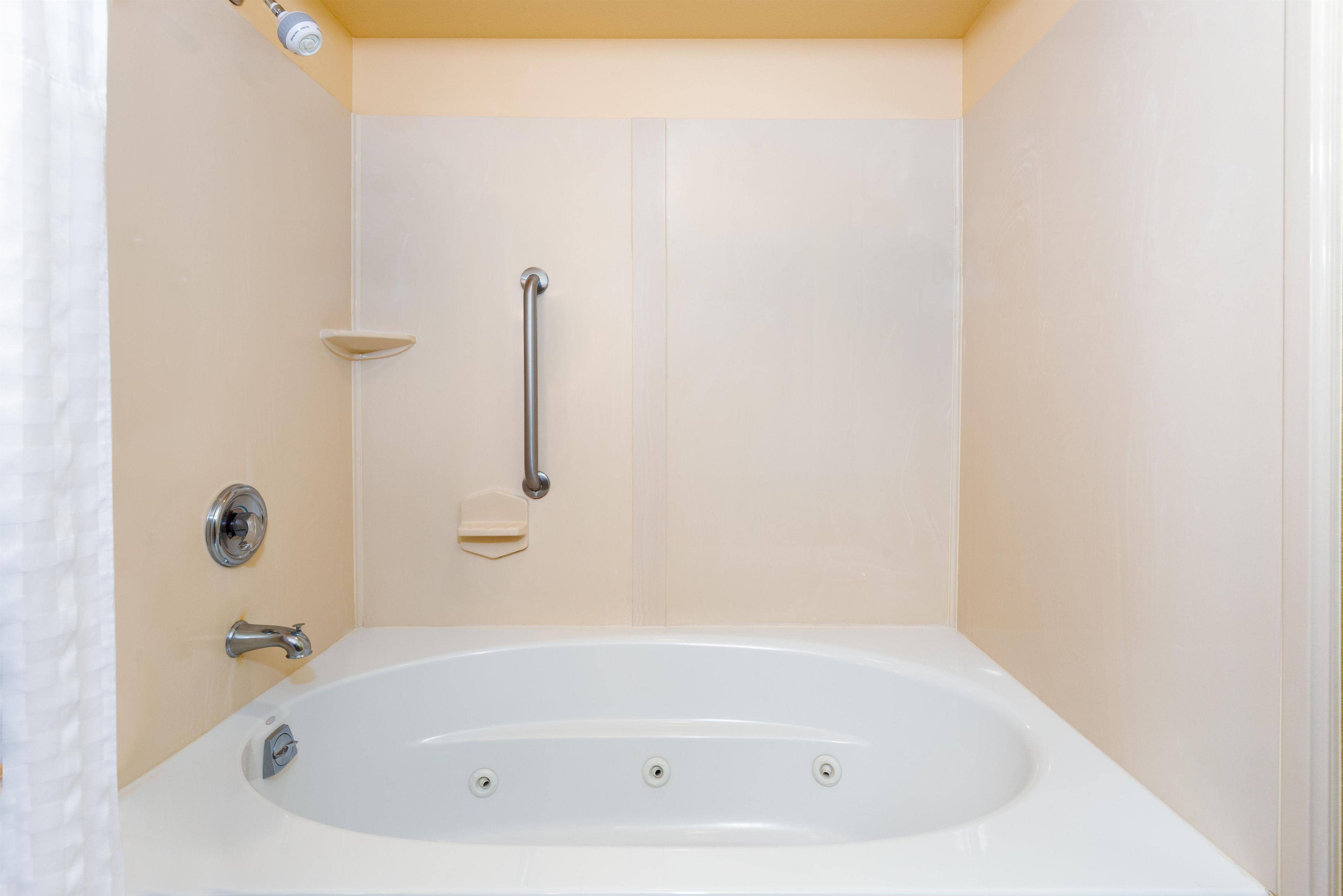 A bathroom with a white bathtub, a handheld showerhead, a wall-mounted faucet, and a soap dish.