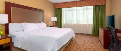 A hotel room with a large bed, a desk, a chair, and a television.