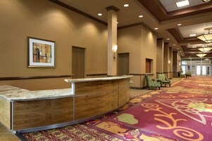 Zona de recepción de un hotel con un mostrador de madera, una obra de arte enmarcada en la pared y una alfombra estampada.