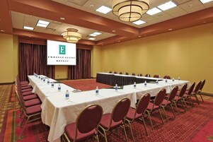 A conference room with a long table, chairs, and a screen displaying the Embassy Suites logo.