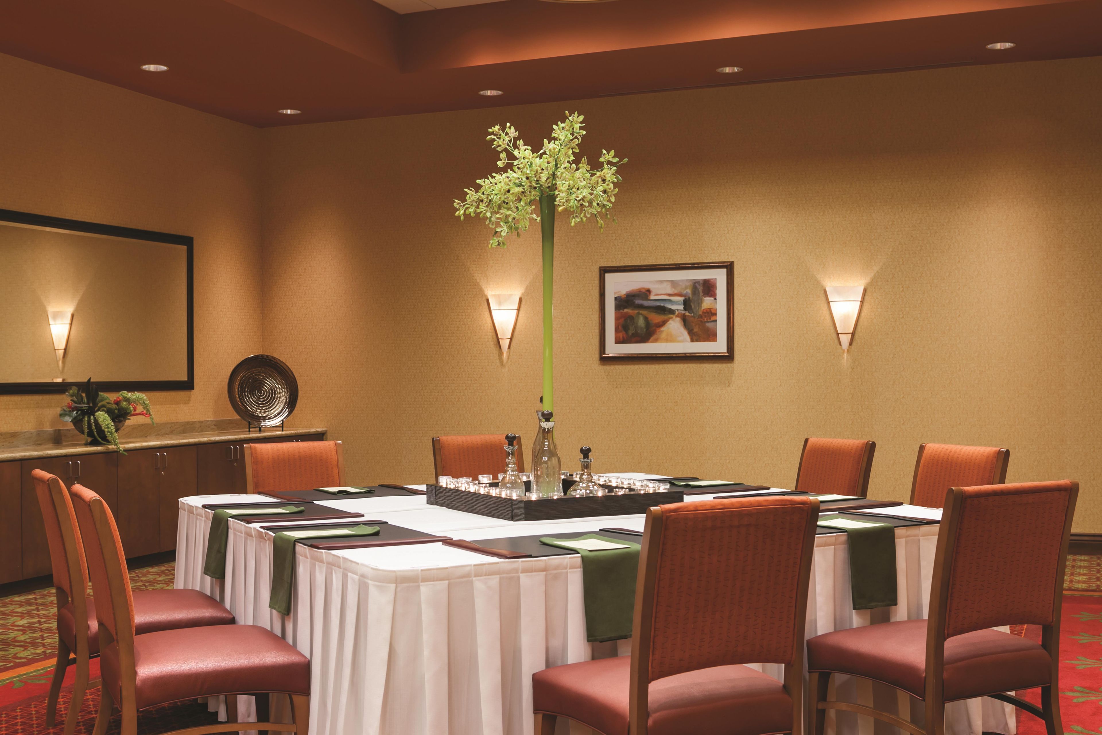 A conference room with a round table, chairs, a plant centerpiece, wall-mounted lights, and a framed picture.