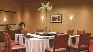 A conference room with a round table, chairs, a plant centerpiece, wall-mounted lights, and a framed picture.
