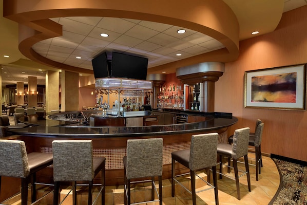 A bar area with a curved counter, multiple bar stools, and a television mounted above the bar.