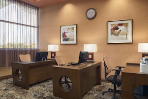 A hotel reception area with two desks, chairs, a clock, and two framed artworks on the wall.