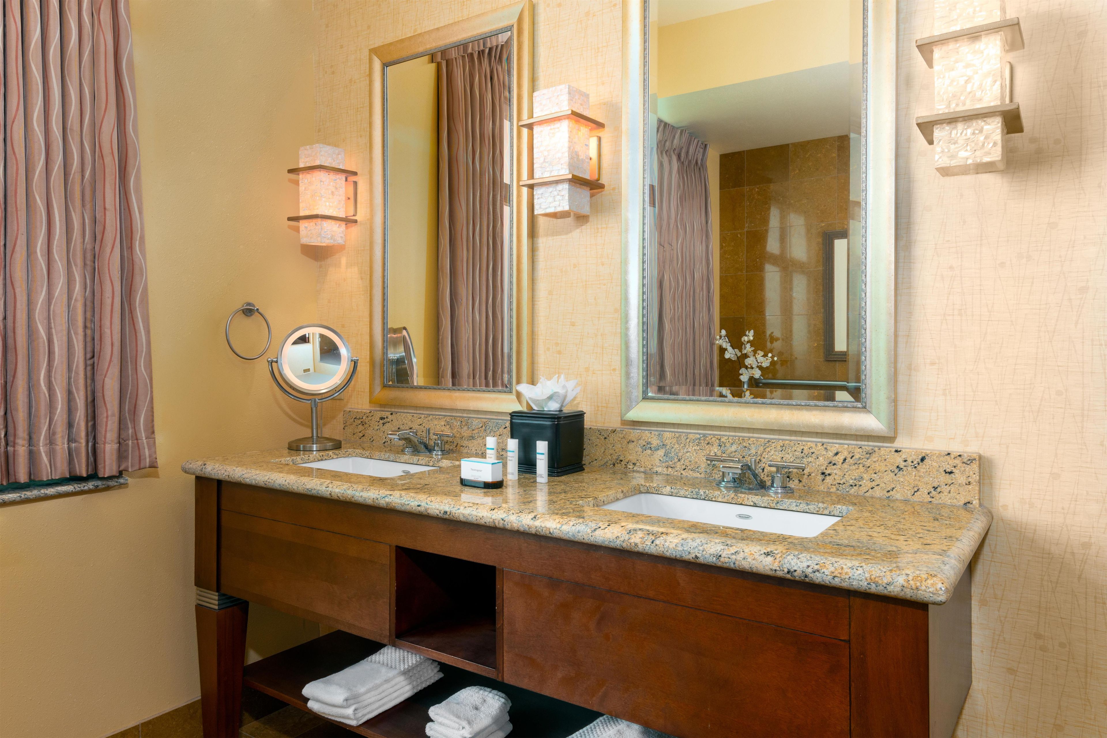 A bathroom with a double sink vanity, a round mirror, a towel rack, and a large mirror above the vanity.