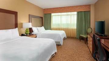 A hotel room with two beds, a desk, a chair, a television, and a window with curtains.