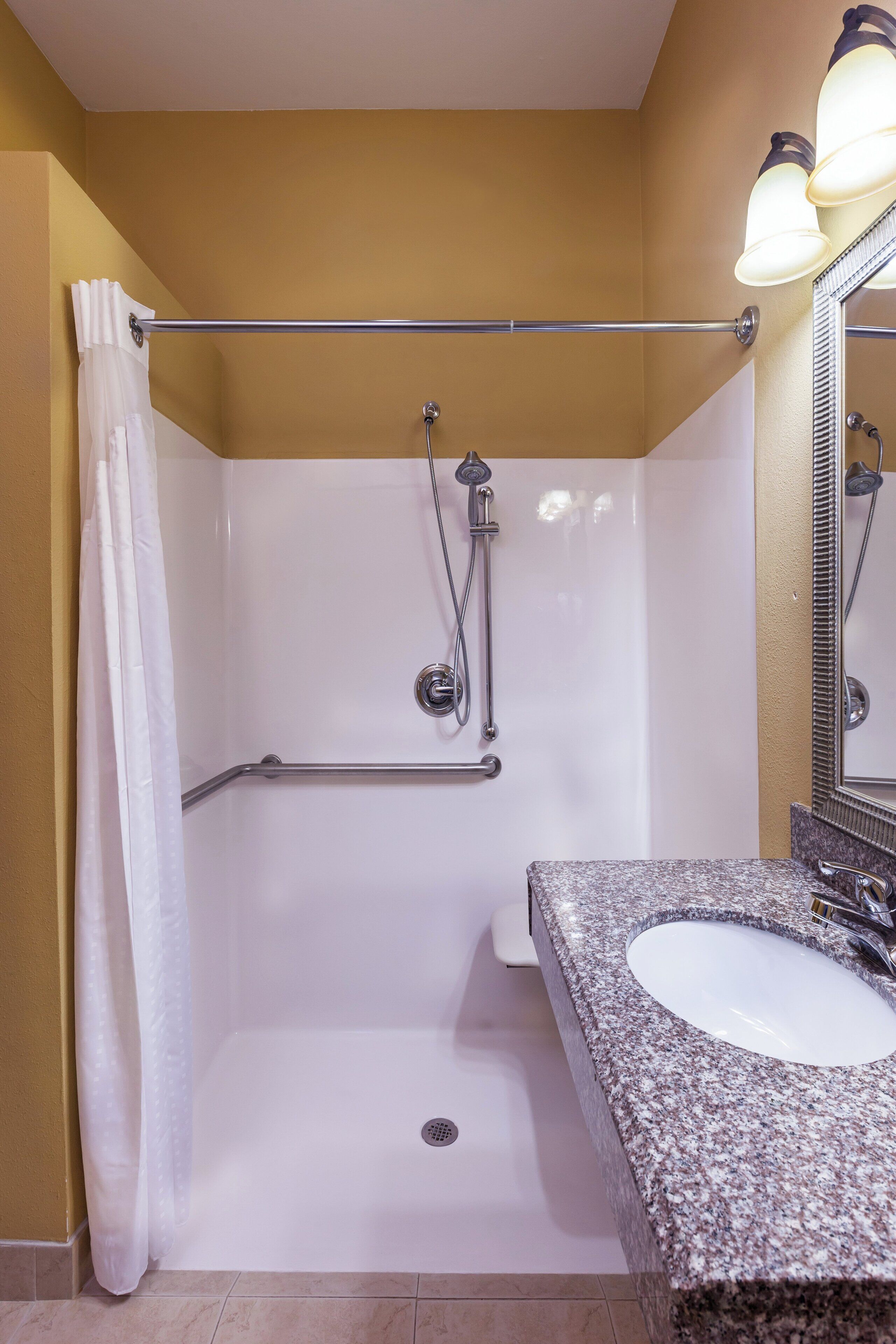 A bathroom with a shower, grab bar, and a sink with a granite countertop.