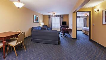 Una habitación de hotel con una mesa de comedor, dos sofás, un televisor y una cama.