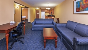 A hotel room with a living area, a kitchenette, a bed, and a desk.