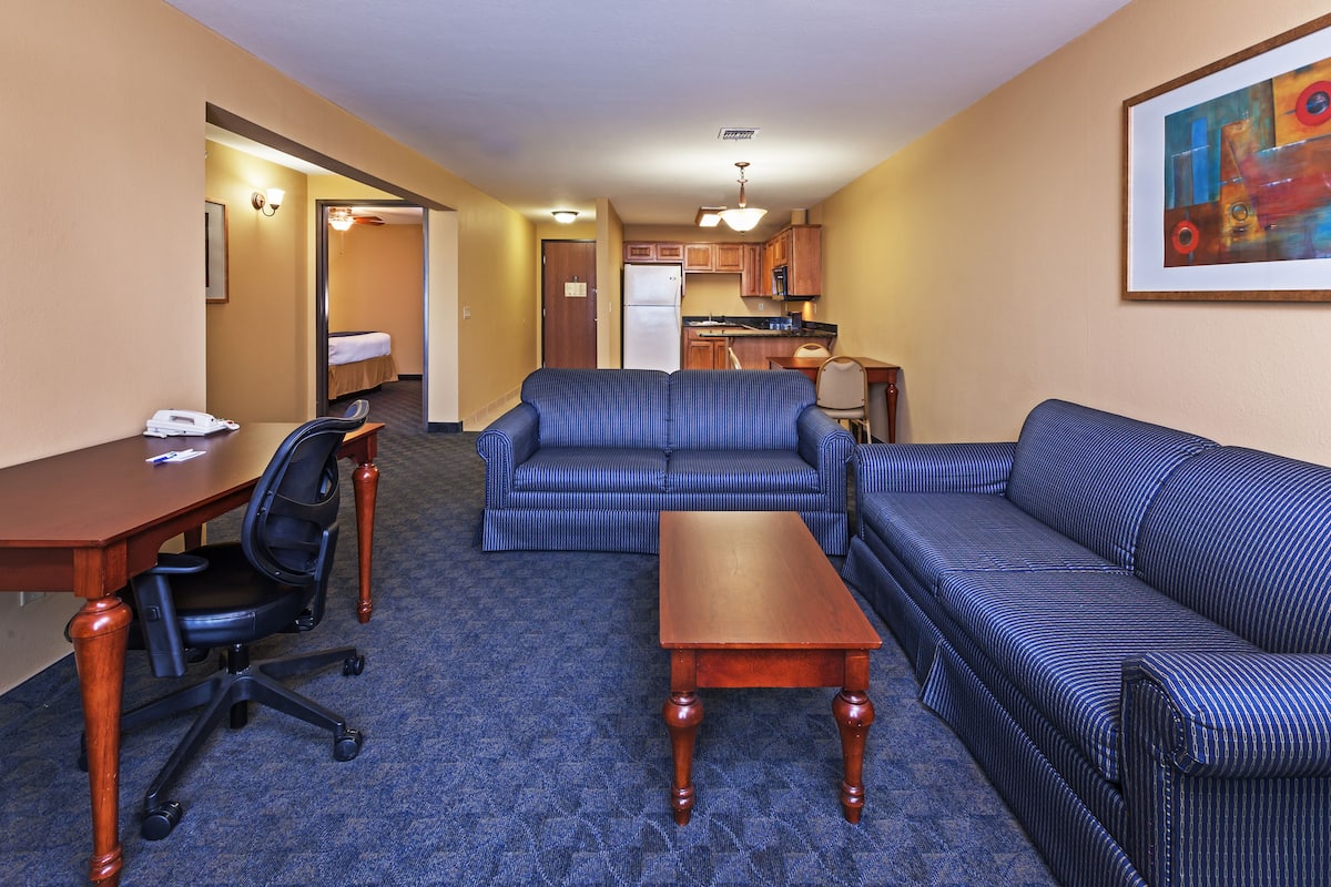A hotel room with a living area, a kitchenette, a bed, and a desk.