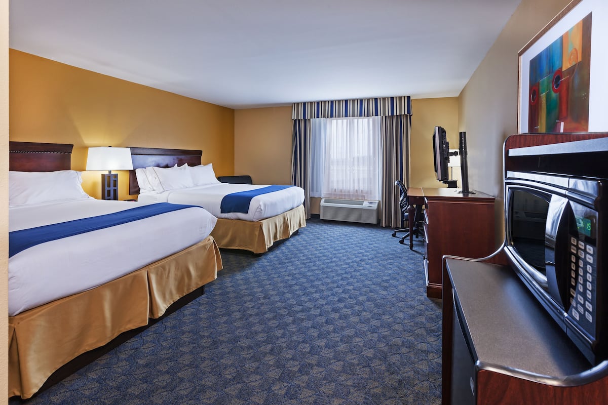 A hotel room with two beds, a desk with a microwave, a TV, and a window with curtains.