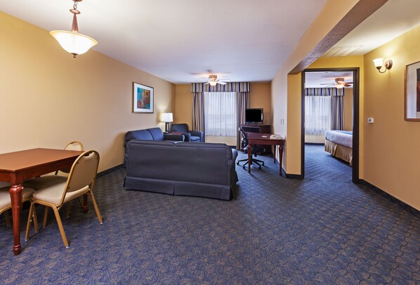 A hotel room with a sofa, a desk, a television, and a dining area with chairs and a table.