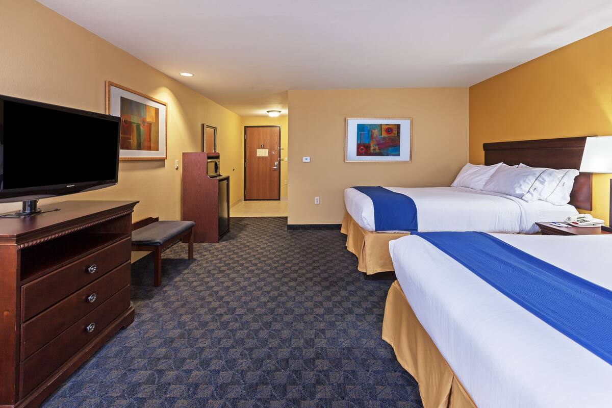 A hotel room with two beds, a television, a desk, and a bench.