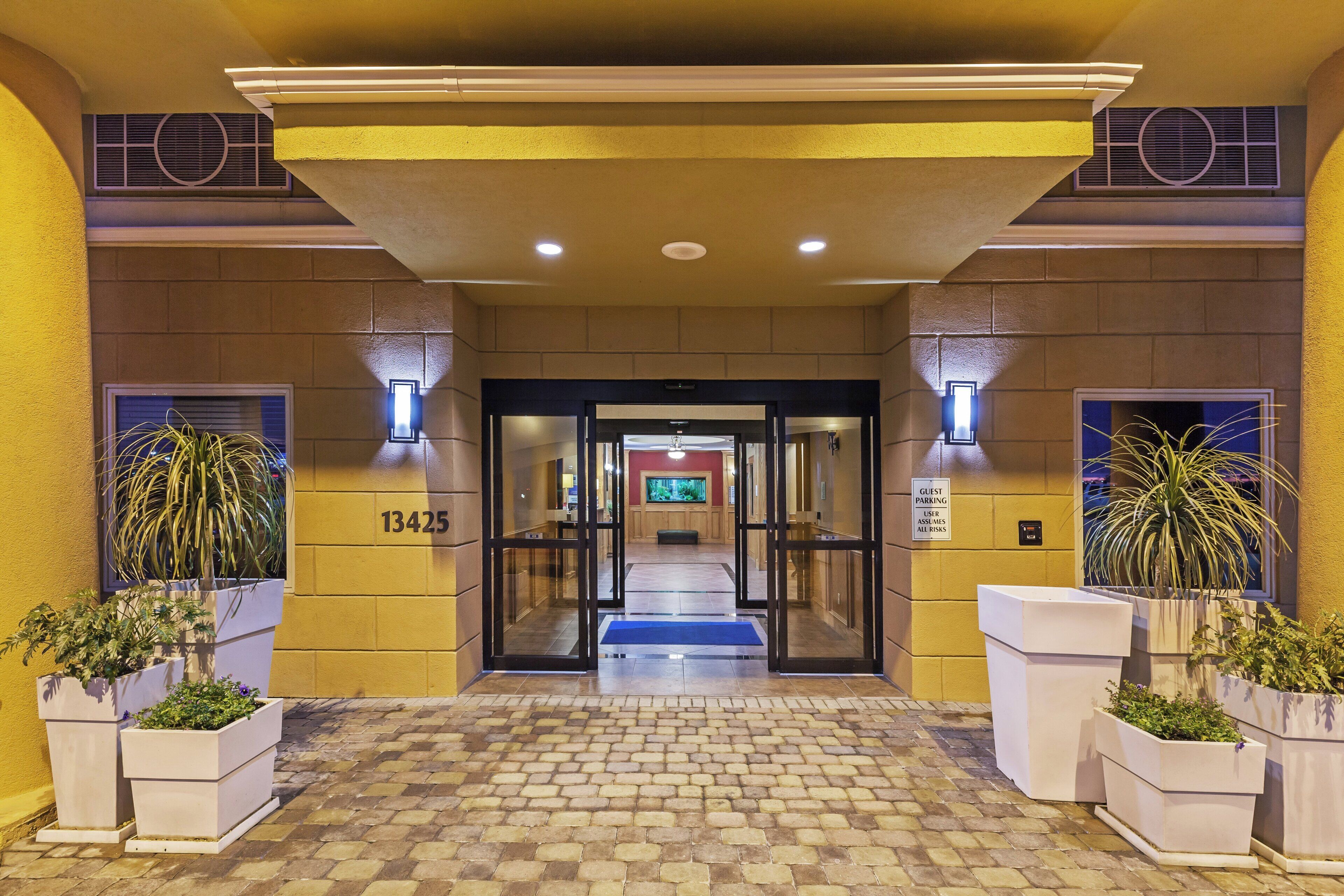 L’entrée d’un hôtel, avec un sol carrelé, un panneau indiquant le numéro de l’établissement et des plantes en pot.