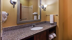 A bathroom with a granite countertop sink, a large mirror, wall-mounted lights, and a towel rack.