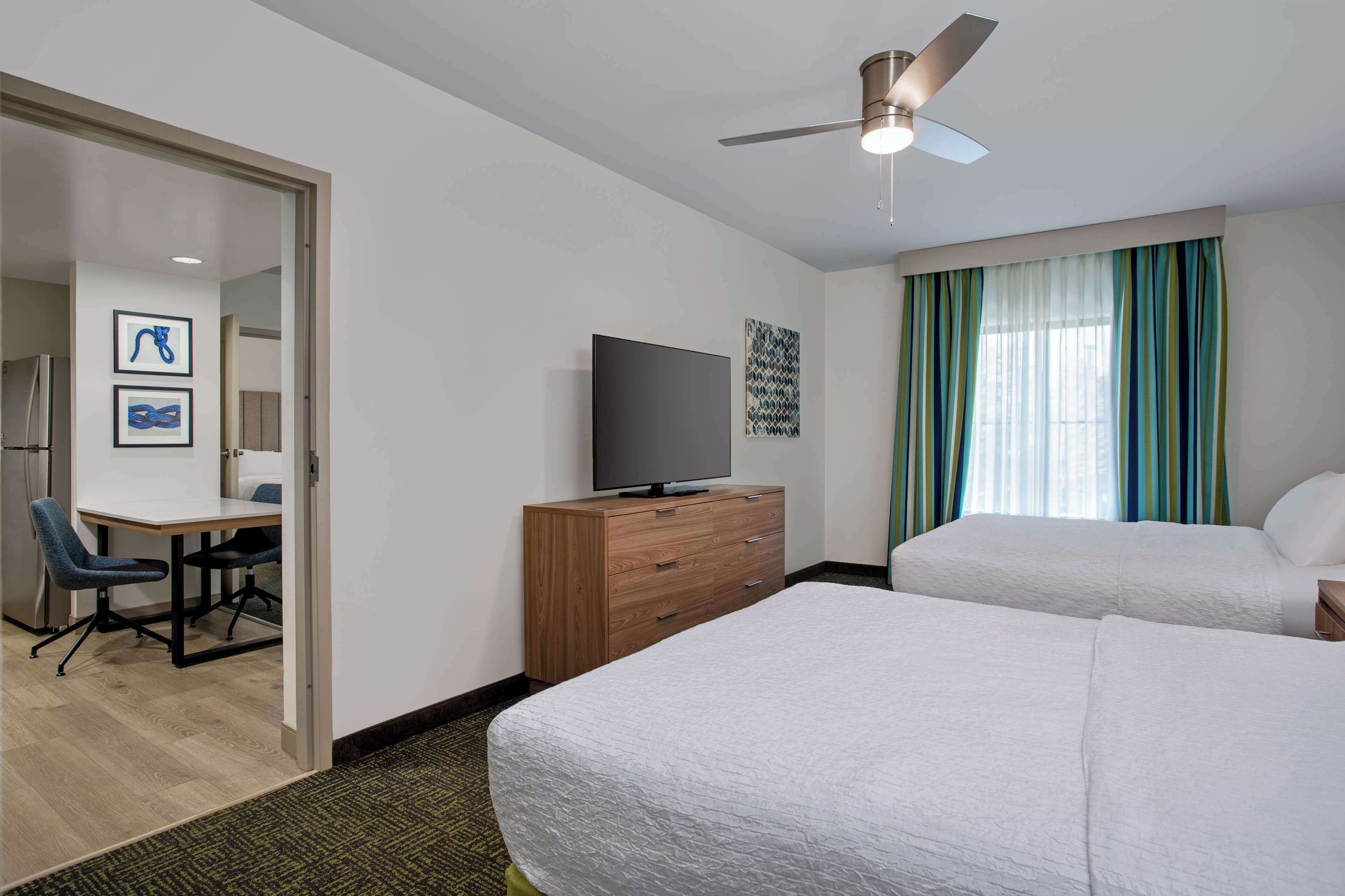 A hotel room with two beds, a desk with a chair, a television, and a ceiling fan.