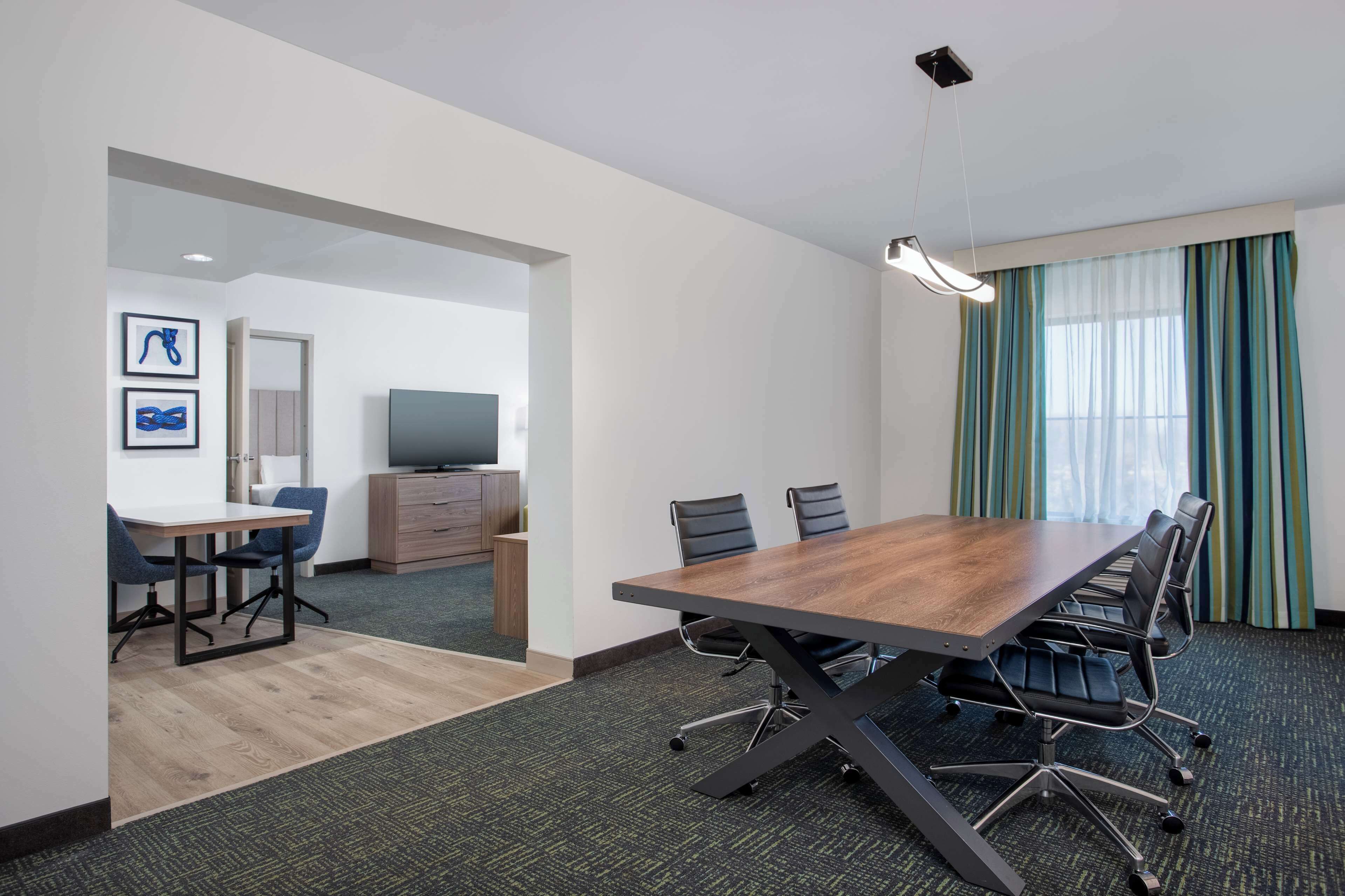 A conference room with a large table, chairs, a television, and a window with curtains.