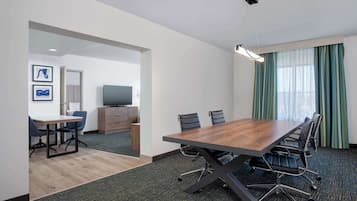 A conference room with a large table, chairs, a television, and a window with curtains.