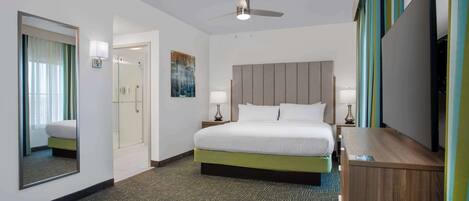 A hotel room with a bed, bedside tables, a mirror, a ceiling fan, and a TV.