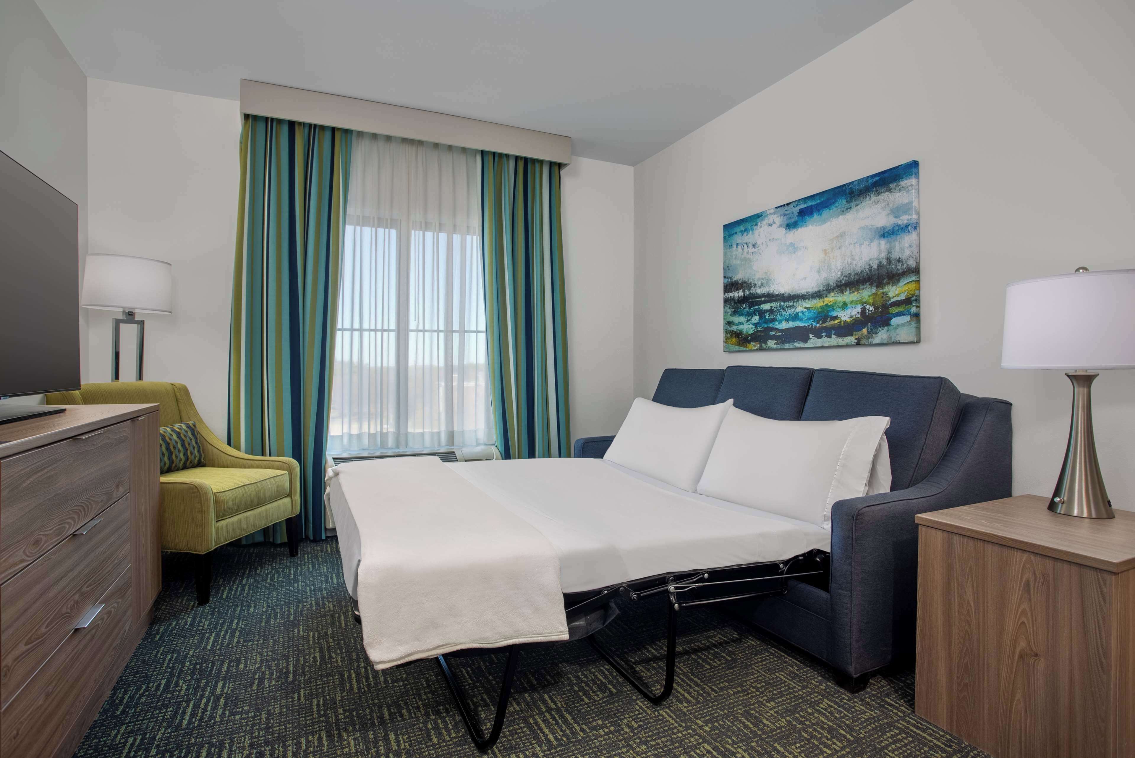A hotel room with a bed, a desk, a chair, a TV, and a painting on the wall.