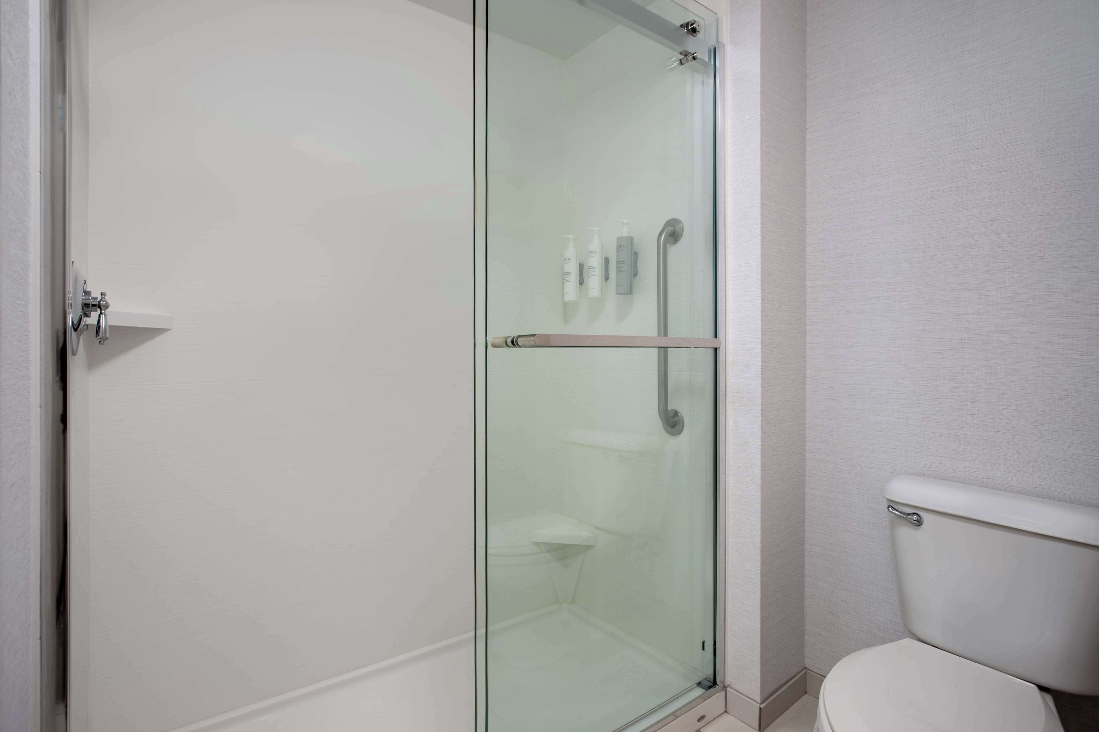 A modern bathroom with a glass-enclosed shower, a toilet, and a small shelf with toiletries.