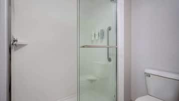 A modern bathroom with a glass-enclosed shower, a toilet, and a small shelf with toiletries.