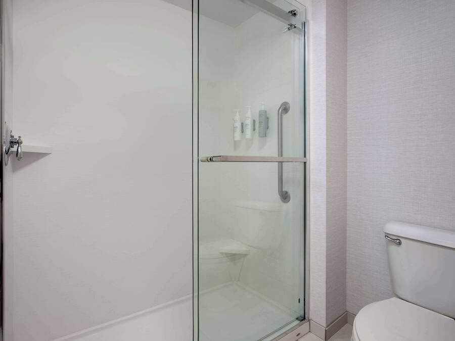 A modern bathroom with a glass-enclosed shower, a toilet, and a small shelf with toiletries.