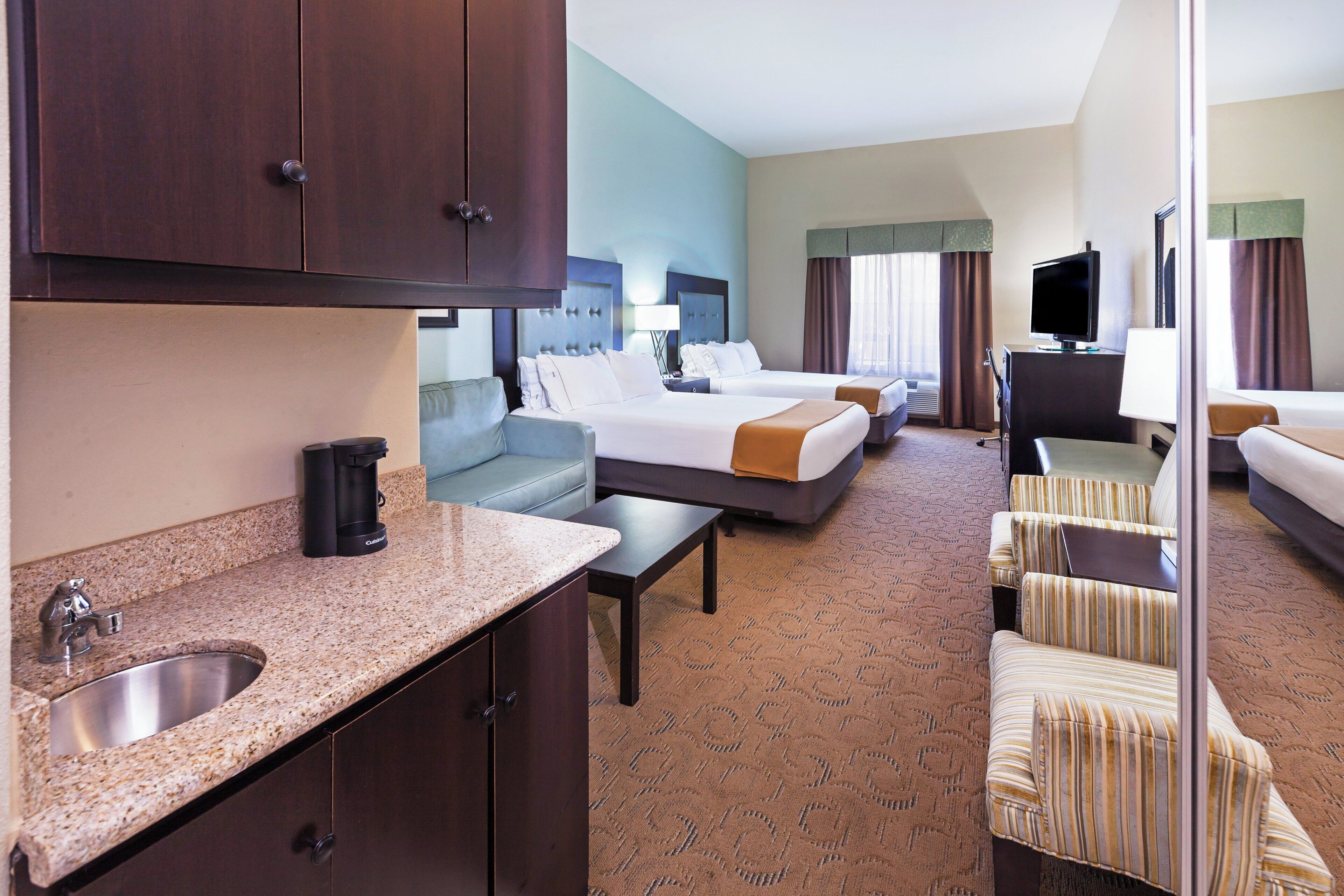 A hotel room with a kitchenette, a bed, a sofa, a television, and a bathroom.