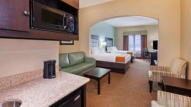 A hotel room with a kitchenette, a green sofa, a bed with two pillows, a desk, and a striped armchair. - Holiday Inn Express Hotel & Suites Victoria by IHG (Victoria)