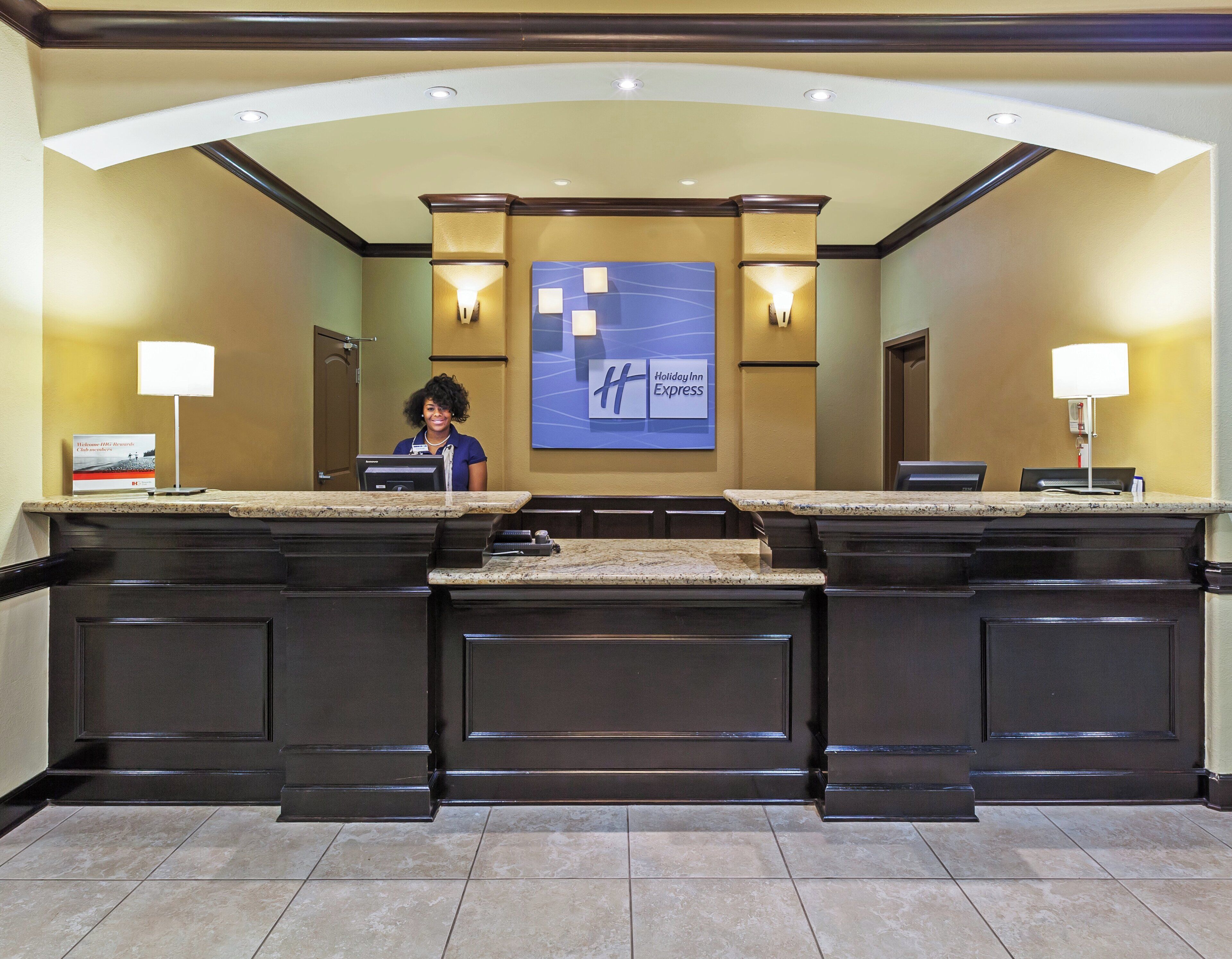 Mostrador de recepción con el letrero de Holiday Inn Express, un monitor de computadora y una mesa para el registro de huéspedes.