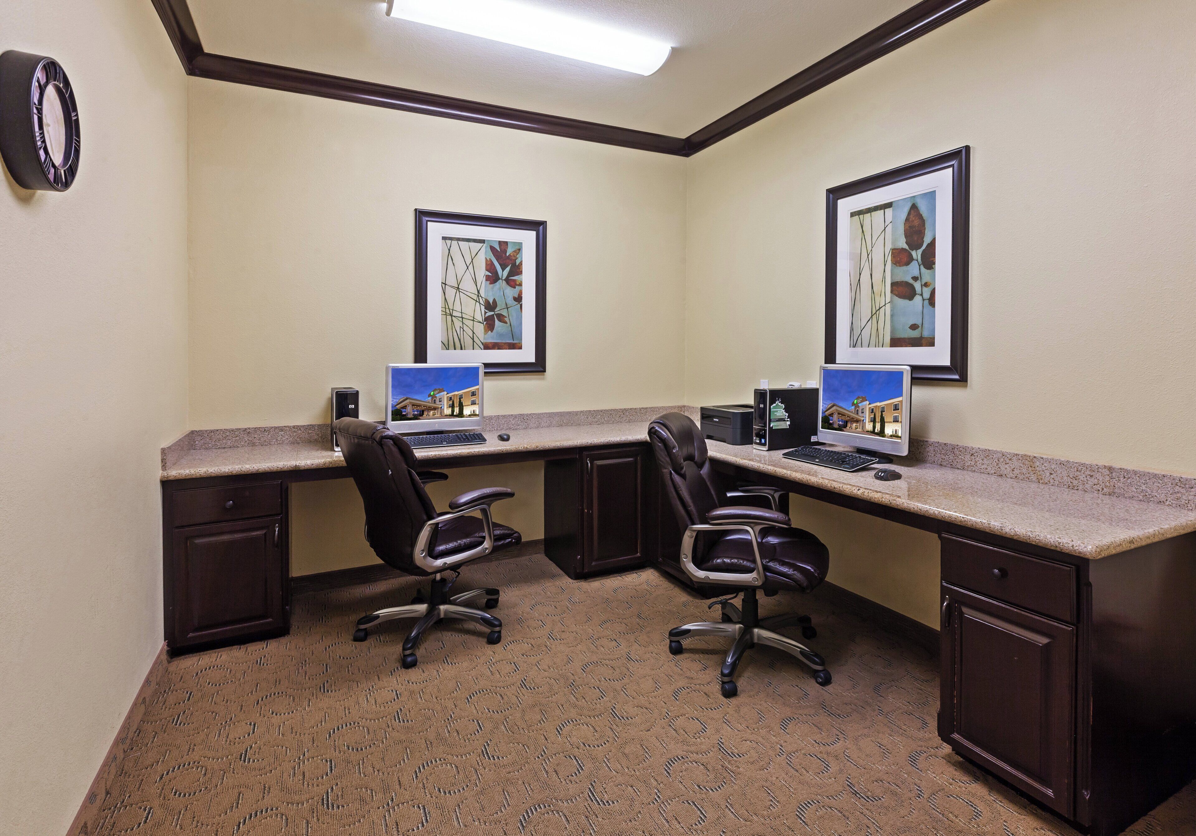 A conference room with two desks, chairs, a clock, and framed artwork on the walls.