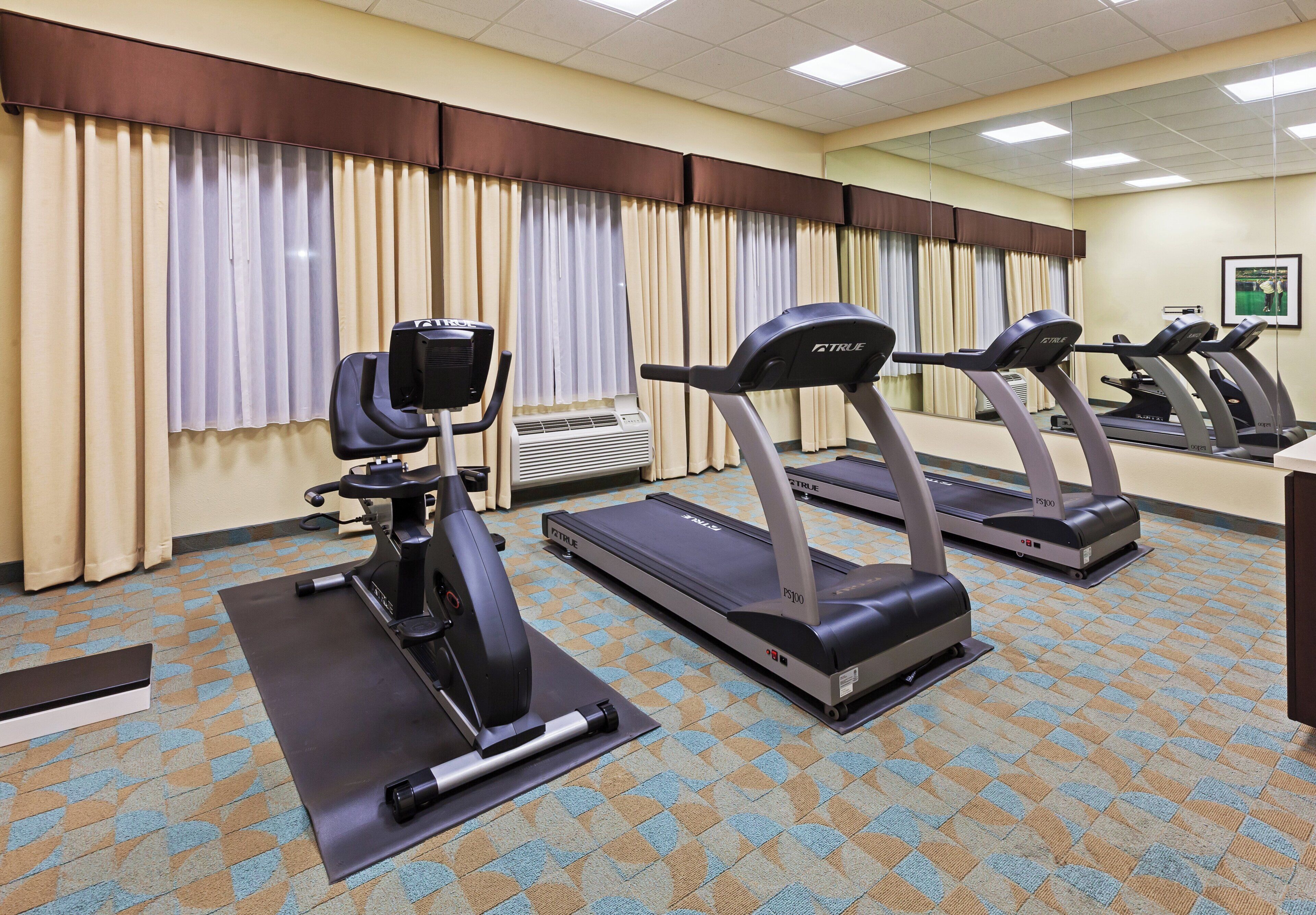 A fitness room with stationary bikes, treadmills, and a mirrored wall.