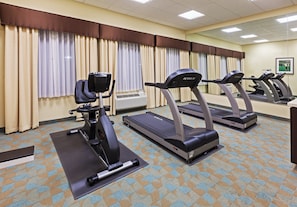 Gimnasio con bicicletas estáticas, cintas de correr y un espejo grande.