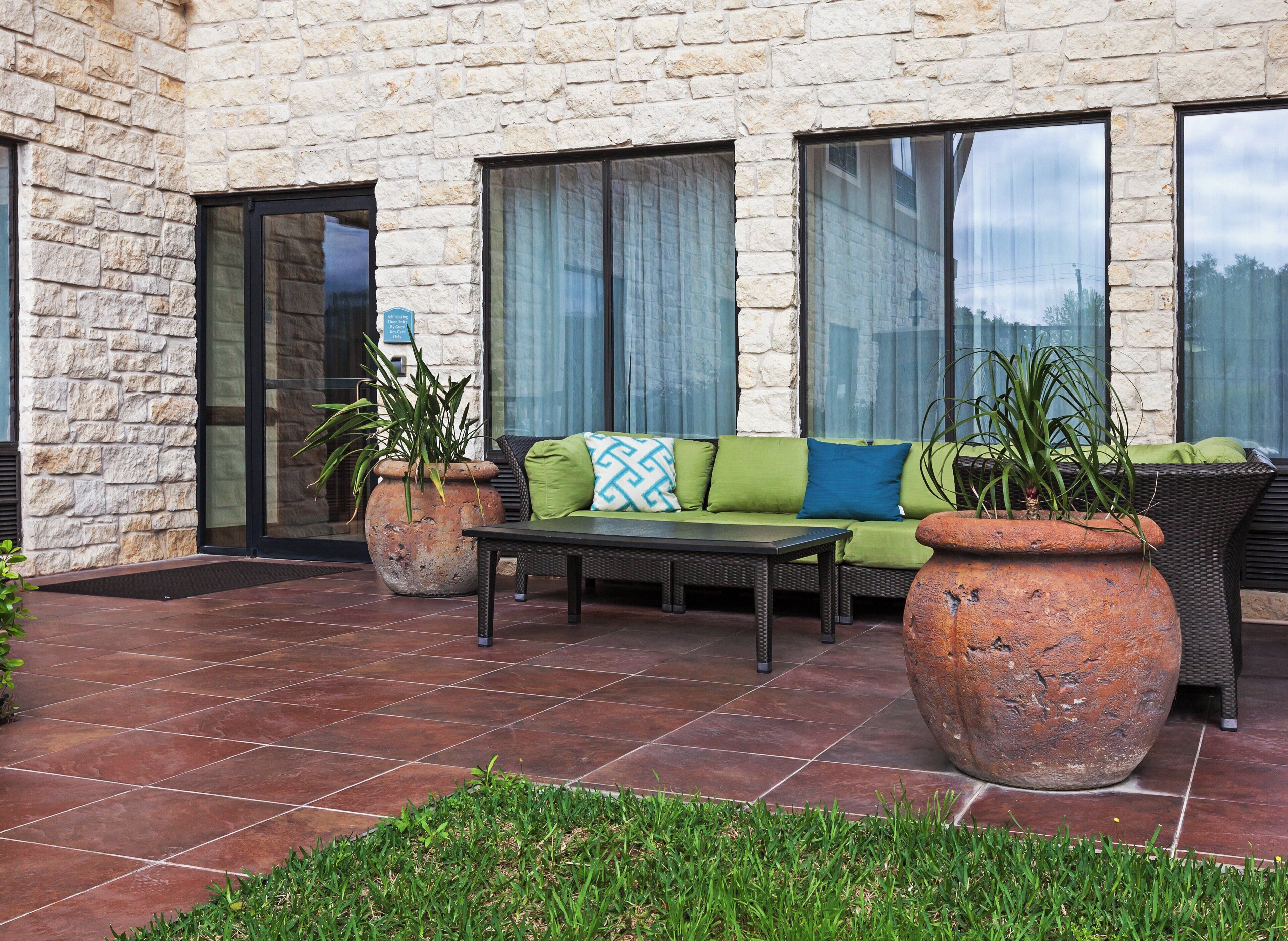 An outdoor seating area with a stone wall, a sofa with cushions, a table, and potted plants.