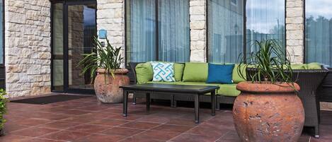 An outdoor seating area with a stone wall, a sofa with cushions, a table, and potted plants.