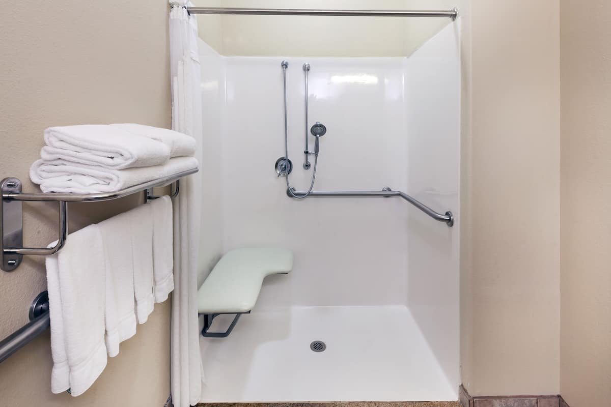 A shower area with a grab bar, a bench, and a towel rack with folded towels.