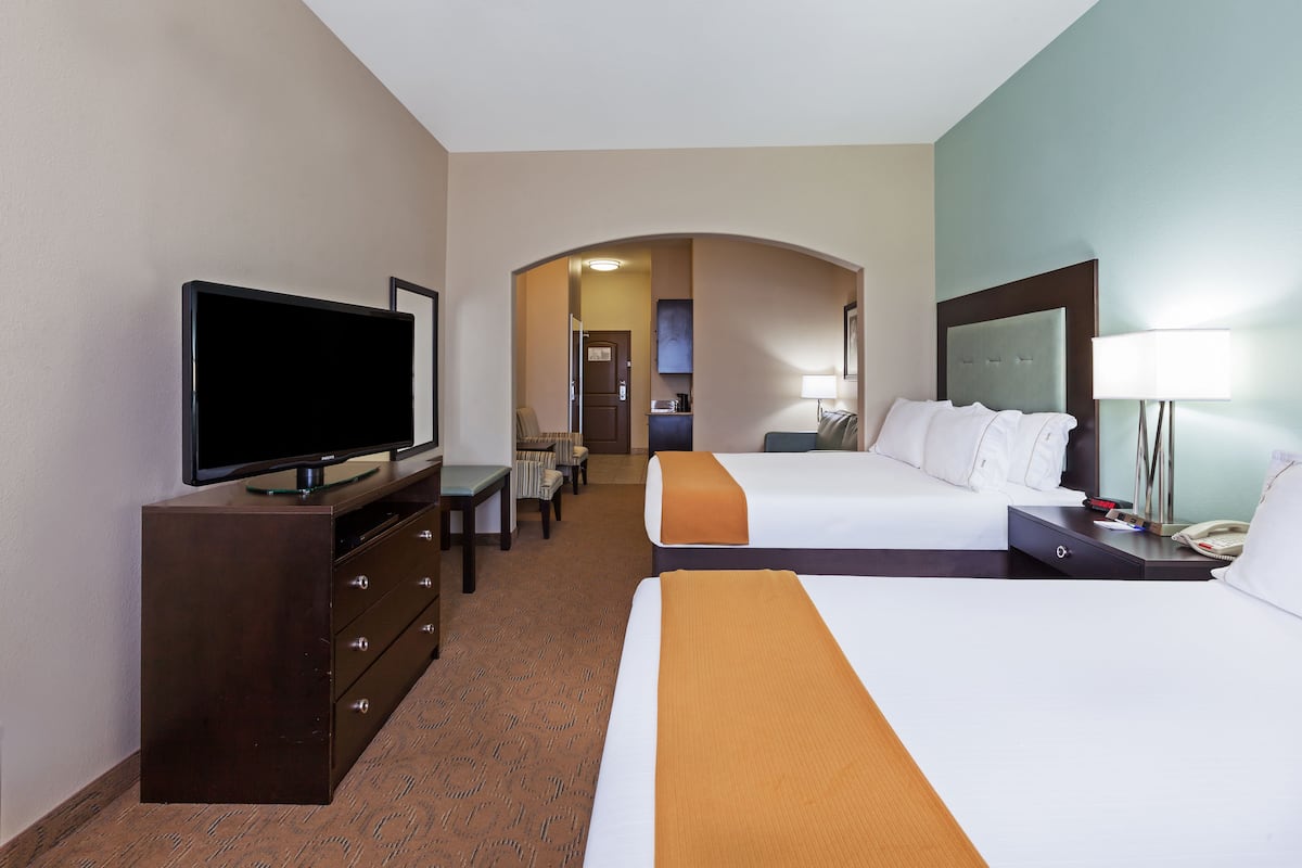 A hotel room with a TV, two beds, a desk, and a bathroom visible through an archway.