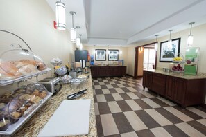 A hotel kitchen with a checkered floor, a buffet area with various food items, and a counter with a fruit display.