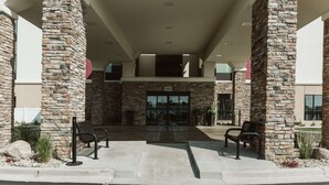 Una entrada de edificio con pilares de piedra, un corredor cubierto y dos bancos.