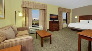 A hotel room with a sofa, a bed, a TV, a desk, and a window with curtains.