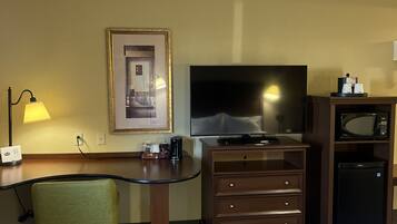 Een hotelkamer met een bureau, stoel, televisie, minibar en een bed.