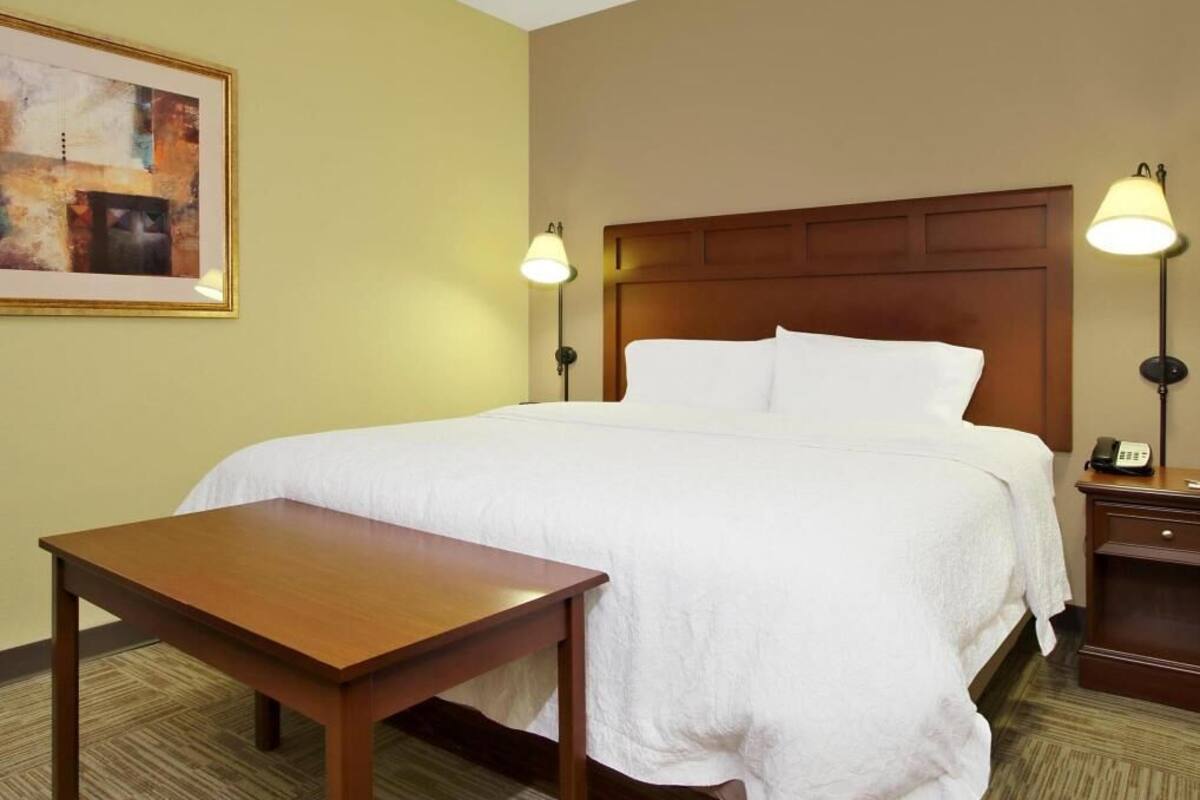 A hotel room with a bed, bedside tables, a lamp, and a painting on the wall.