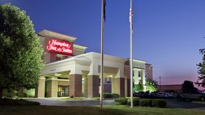 A Hampton Inn & Suites hotel with a prominent neon sign, a parking lot, and a flagpole.