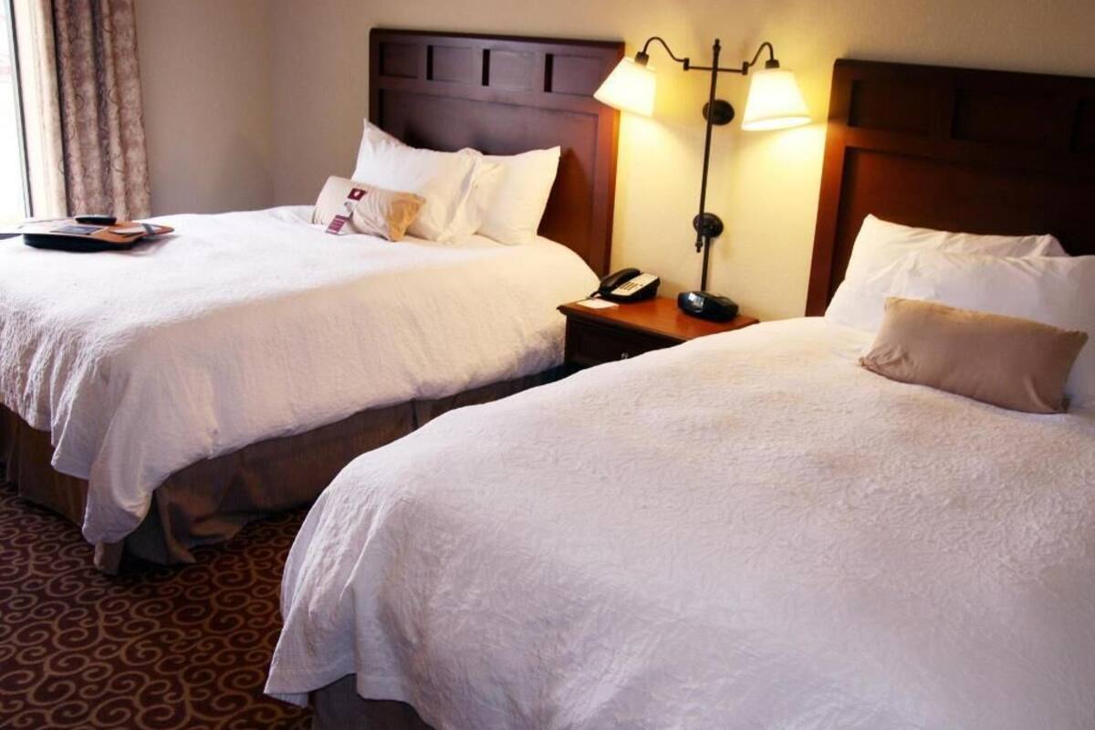 Two beds with white linens, a wooden headboard, bedside lamps, and a patterned carpet.