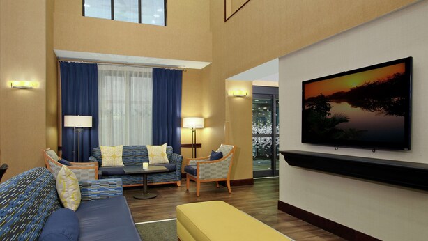 A hotel room with a large bed, a sofa, a chair, a TV, and a window with curtains.