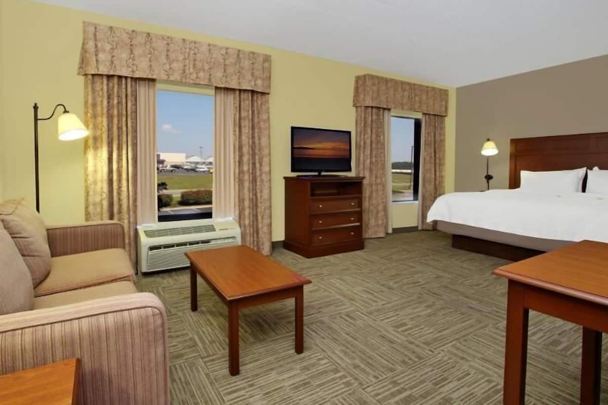 A hotel room with a bed, a TV, a desk, a chair, and a window with curtains.