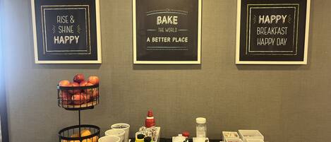 A breakfast buffet setup with various food items and condiments, accompanied by inspirational wall art.