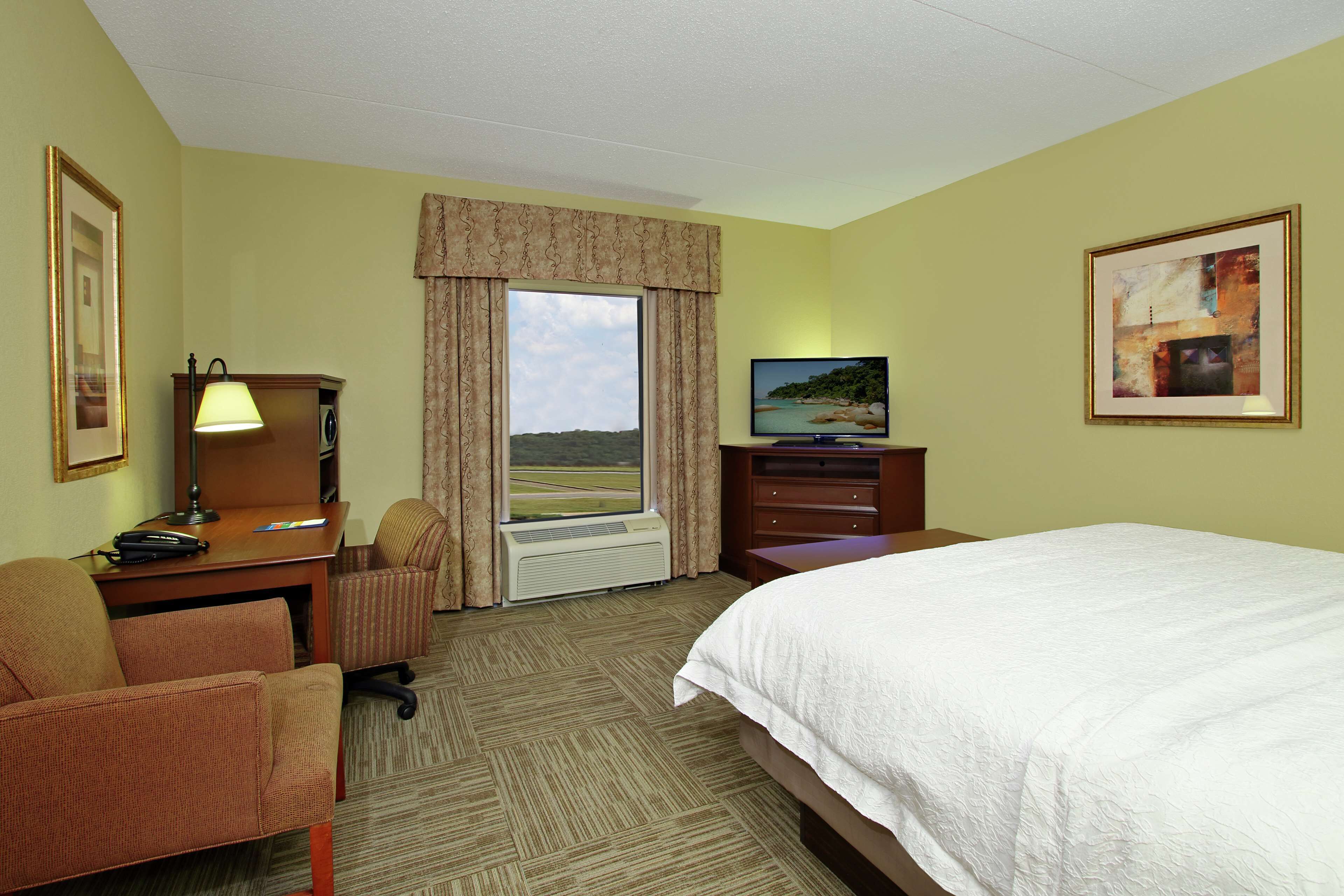 A hotel room with a bed, desk, chair, and a large window offering a view.