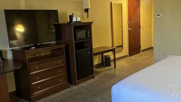 A hotel room with a bed, a desk with a flat-screen TV, a microwave, a lamp, and a door.