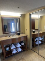Un baño de hotel con dos lavamanos, un espejo grande y repisas con toallas.